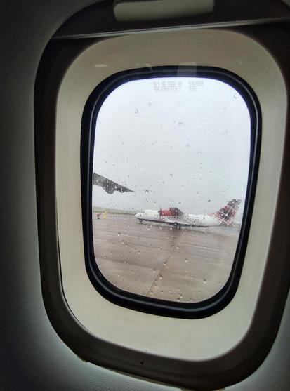 Blick aus einem Flugzeugfenster, Regentropfen auf der Scheibe, draußen ist es grau und nass, nebenan auf dem Rollfeld eine andere Propellermaschine