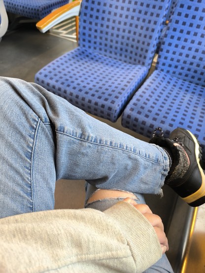 Beine in Jeans und ein Stück Arm von oben fotografiert, deutet Sitzen in einer S Bahn an Beine in Jeans und ein Stück Arm von oben fotografiert, deutet Sitzen in einer S Bahn an